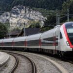 Viaggiatori salgono su un treno passeggeri in una stazione ferroviaria italiana.